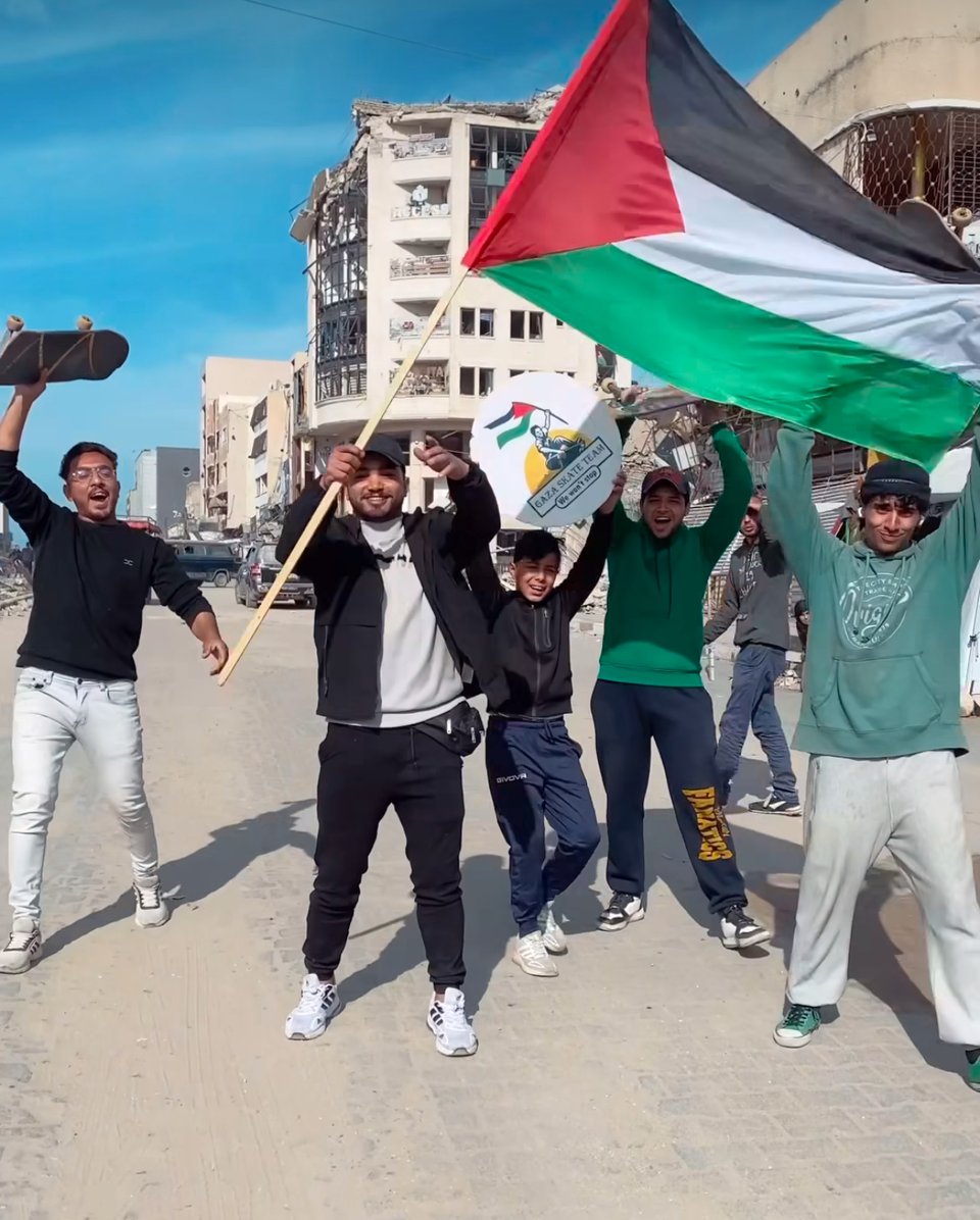 a group of young men with skateboard waving a large palestinian flag