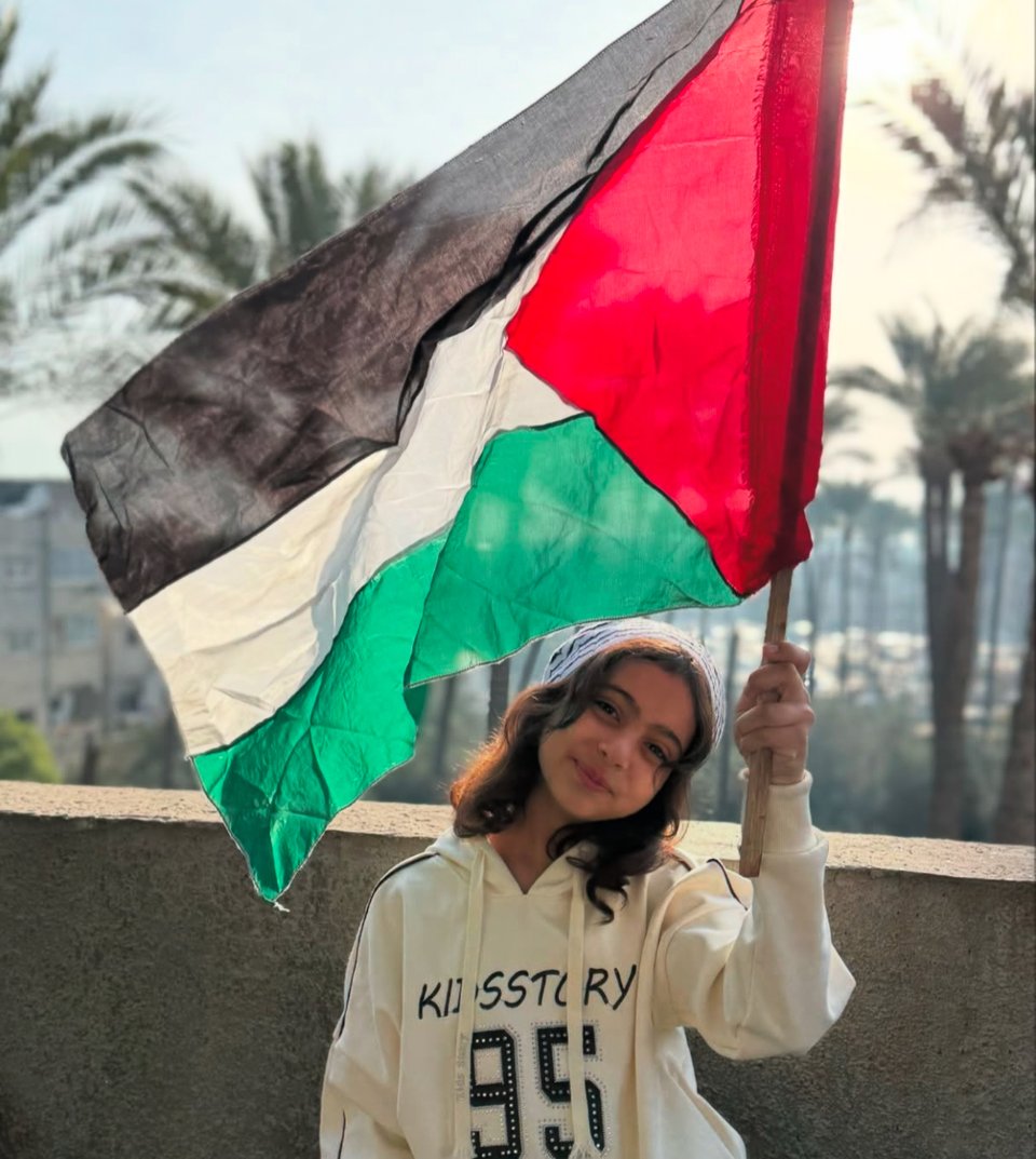 a young girl renad waving a palestinian flag on a balcony